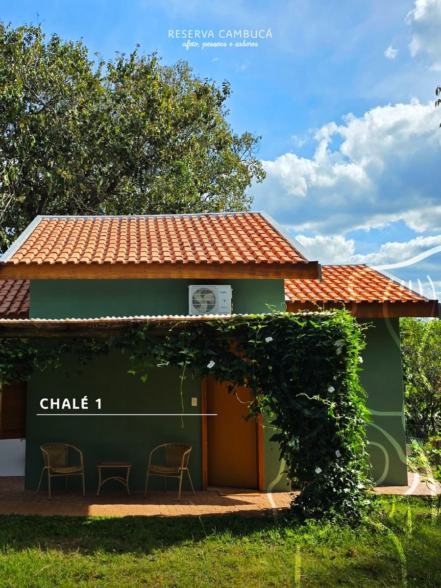 Fachada verde do Chalé 1 da Pousada Reserva Cambucá, com varanda, cadeiras e telhado de barro