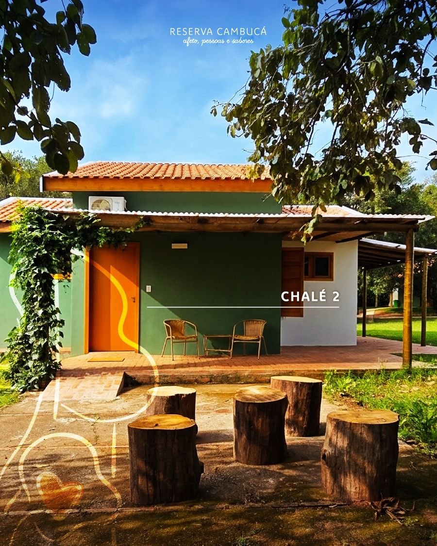 Fachada do Chalé 2 da Pousada Reserva Cambucá, com porta laranja, varanda e troncos de madeira como bancos