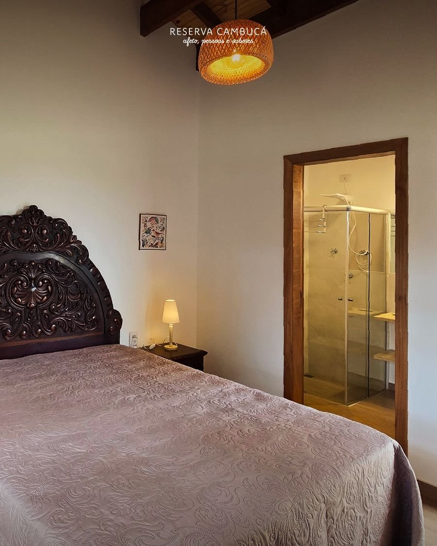 Quarto do Chalé 3 com cama queen, cabeceira de madeira entalhada e luminária de palha