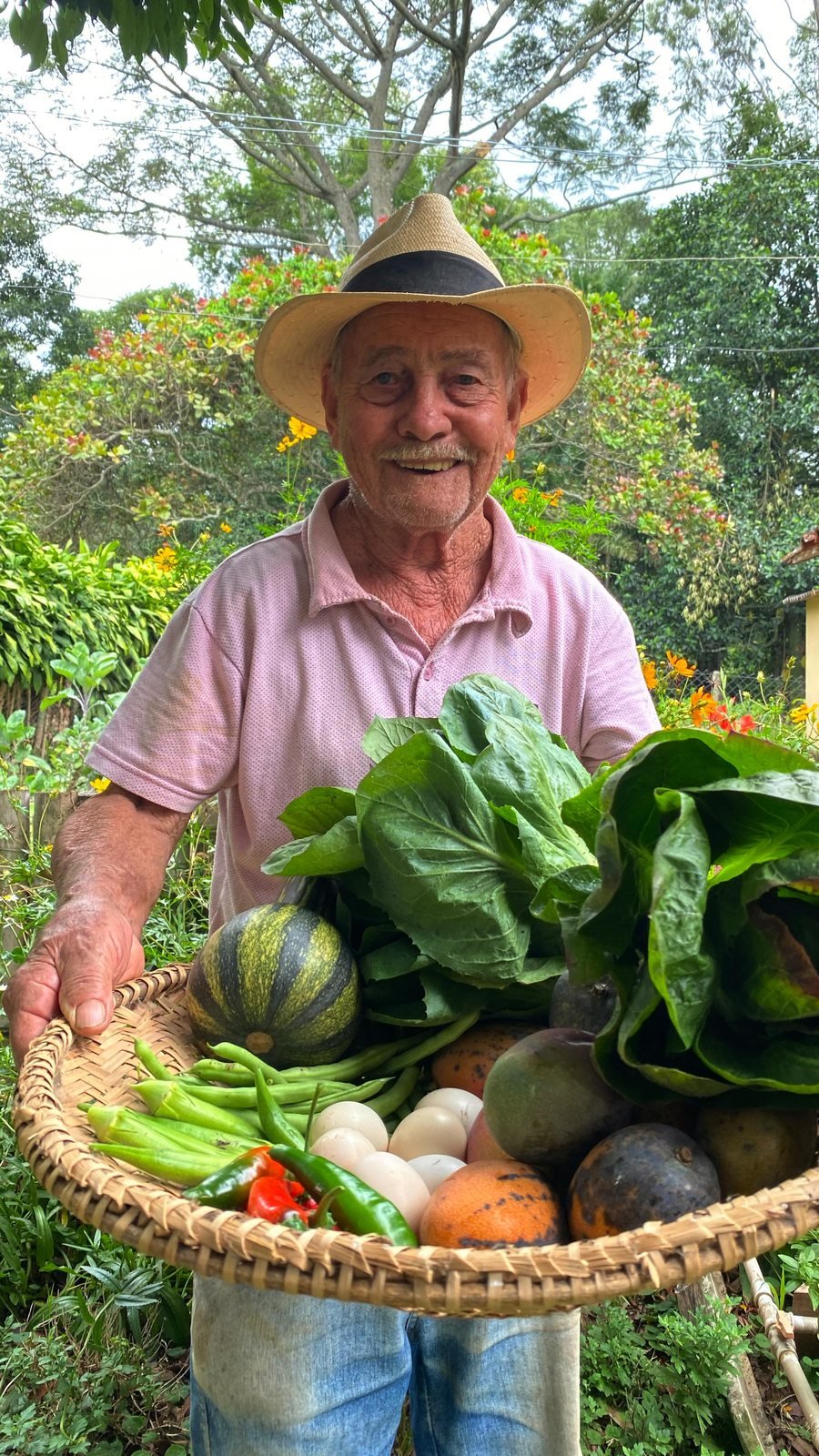 Seu Gentil sorrindo com um cesto de verduras, legumes e ovos colhidos na horta da Pousada Reserva Cambucá