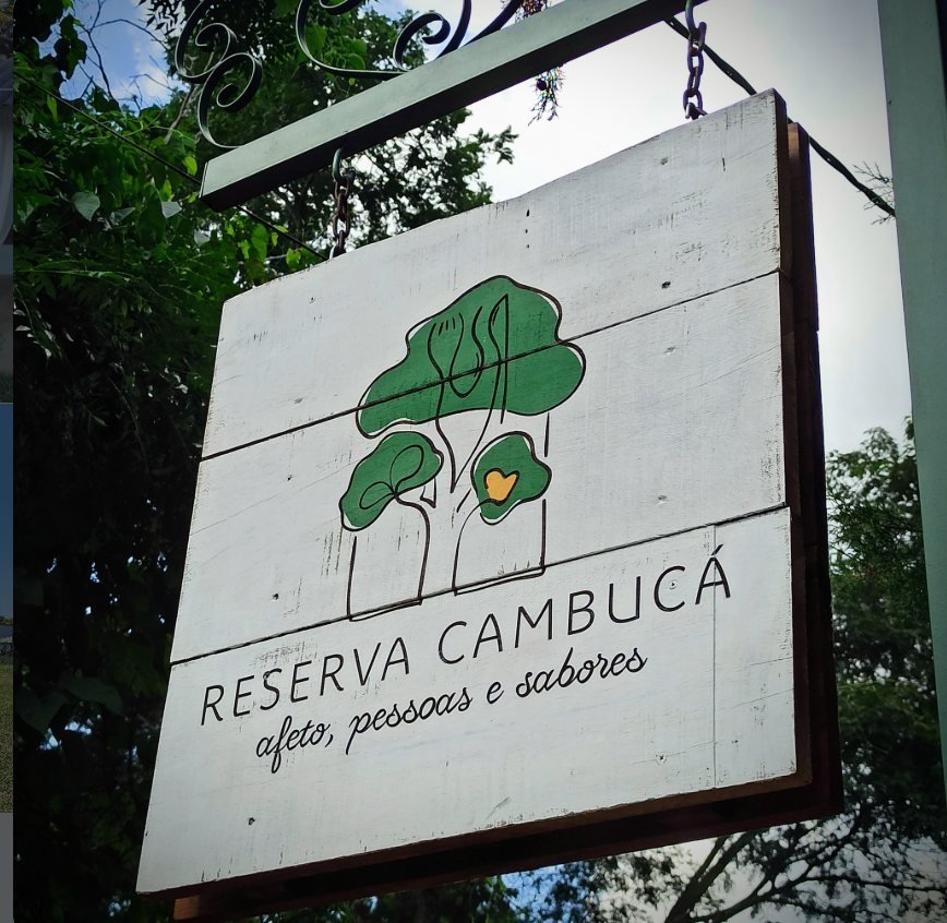 Placa de madeira na entrada da Pousada Reserva Cambucá, com o logotipo da árvore e o nome pintados à mão