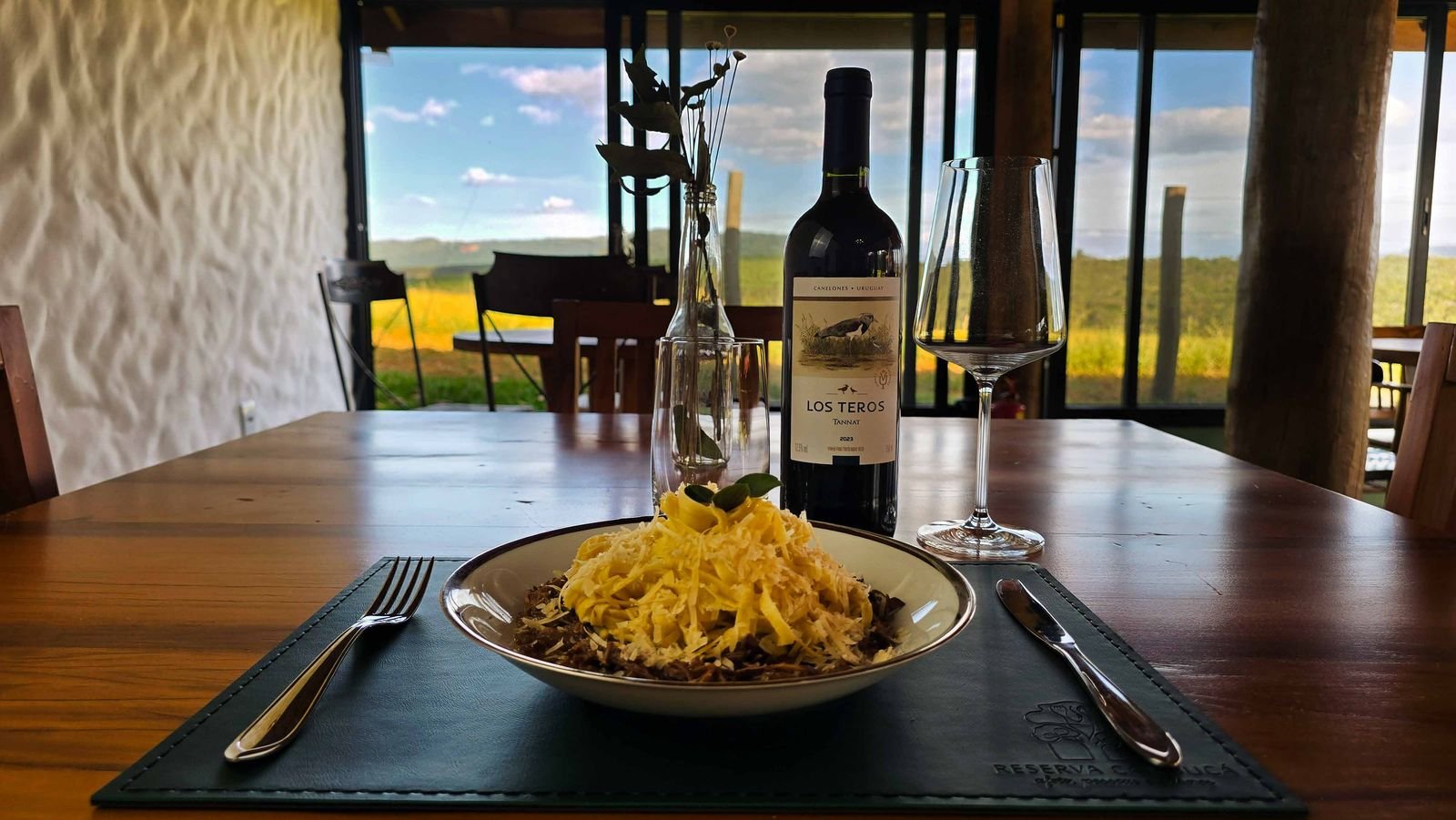 Prato de massa fresca à mesa de madeira, com vinho e vista para a serra no restaurante da Pousada Reserva Cambucá
