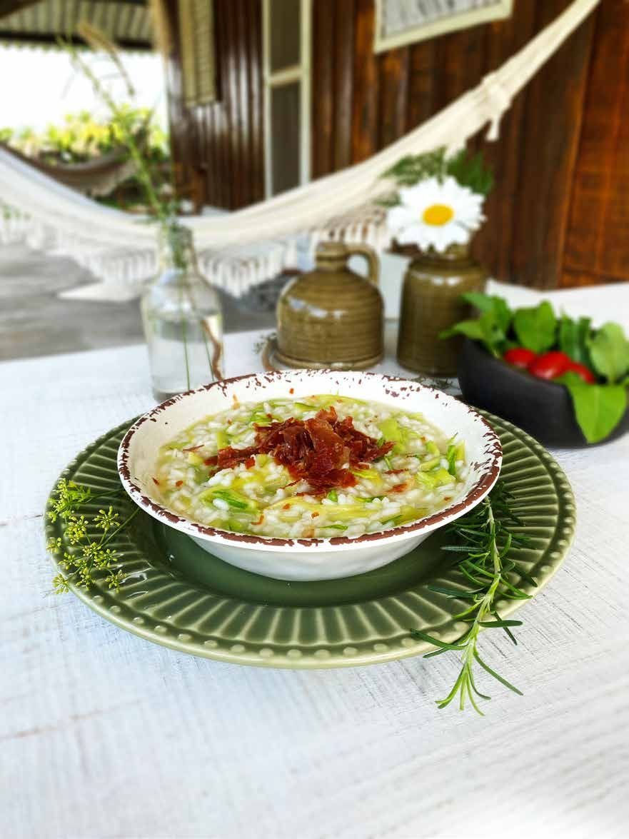 Prato de risoto guarnecido com folhas verdes, sobre prato verde e mesa branca